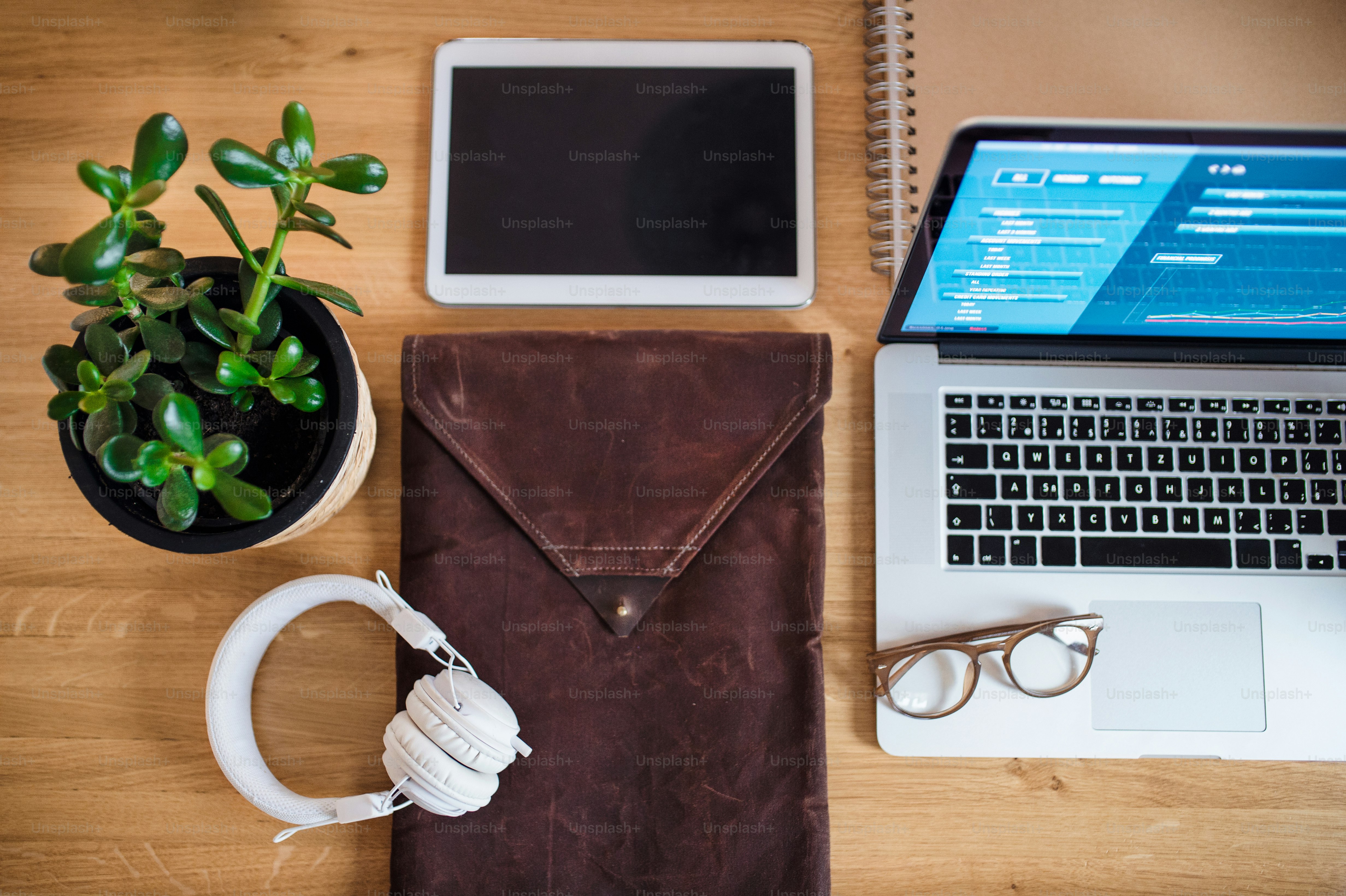Komposisi tablet, laptop, headphone, dan tanaman pot di atas meja, tampilan atas.
