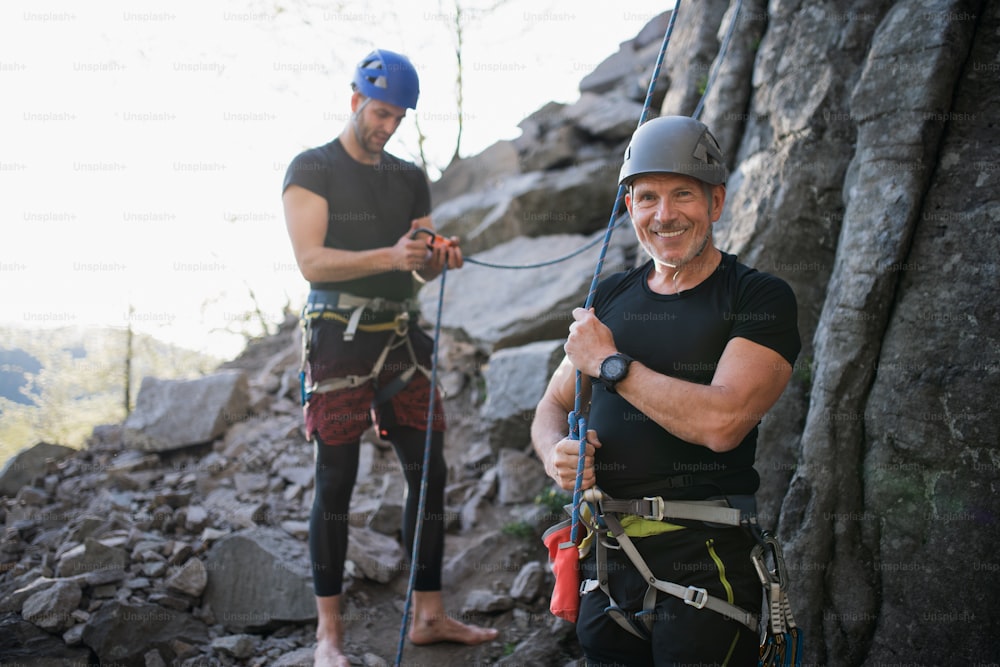 Portrait of senior man with instructor climbing rocks outdoors in nature, active lifestyle.