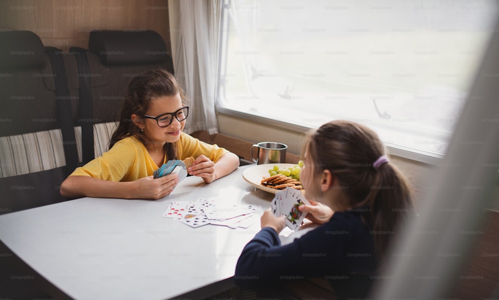Petites filles heureuses jouant aux cartes à l’intérieur dans une caravane, voyage de vacances en famille.