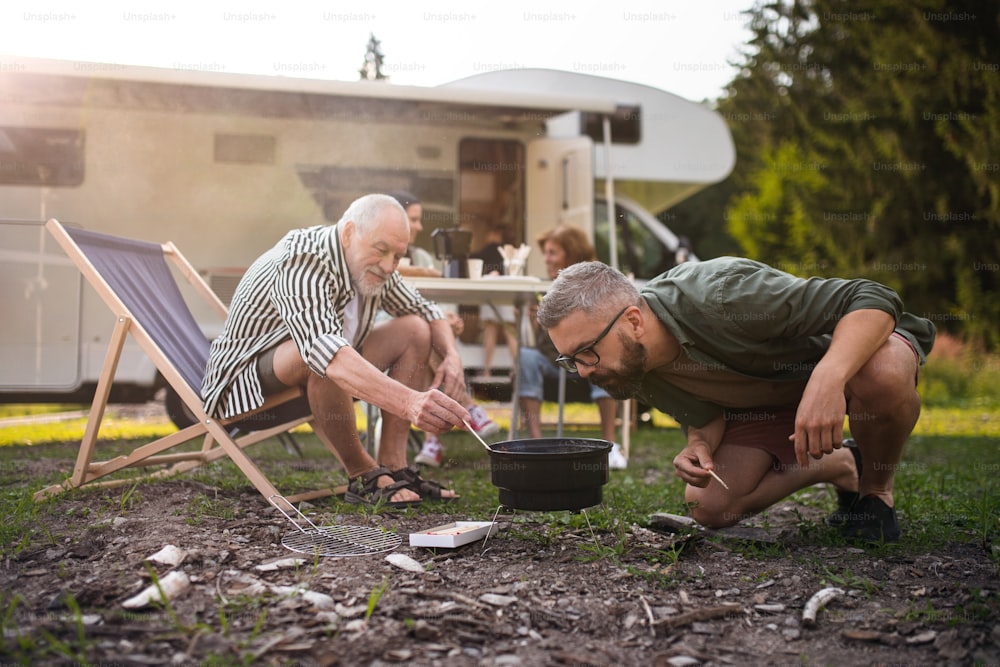 Un homme mûr avec un père âgé préparant un barbecue au camping en plein air, un voyage de vacances en famille en caravane.