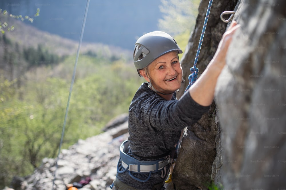 Portrait of senior woman climbing rocks andlooking at camera outdoors in nature, active lifestyle.