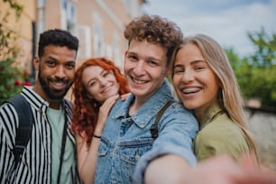 A portrait of group of young people outdoors on trip in town, taking selfie and looking at camera.