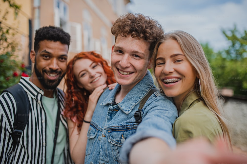 Un retrato de un grupo de jóvenes al aire libre en viaje por la ciudad, tomándose selfies y mirando a la cámara.