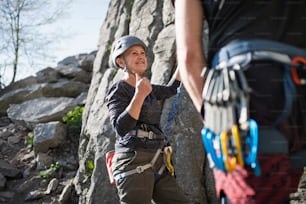 Senior woman with unrecognizable instructor climbing rocks outdoors in nature, active lifestyle.