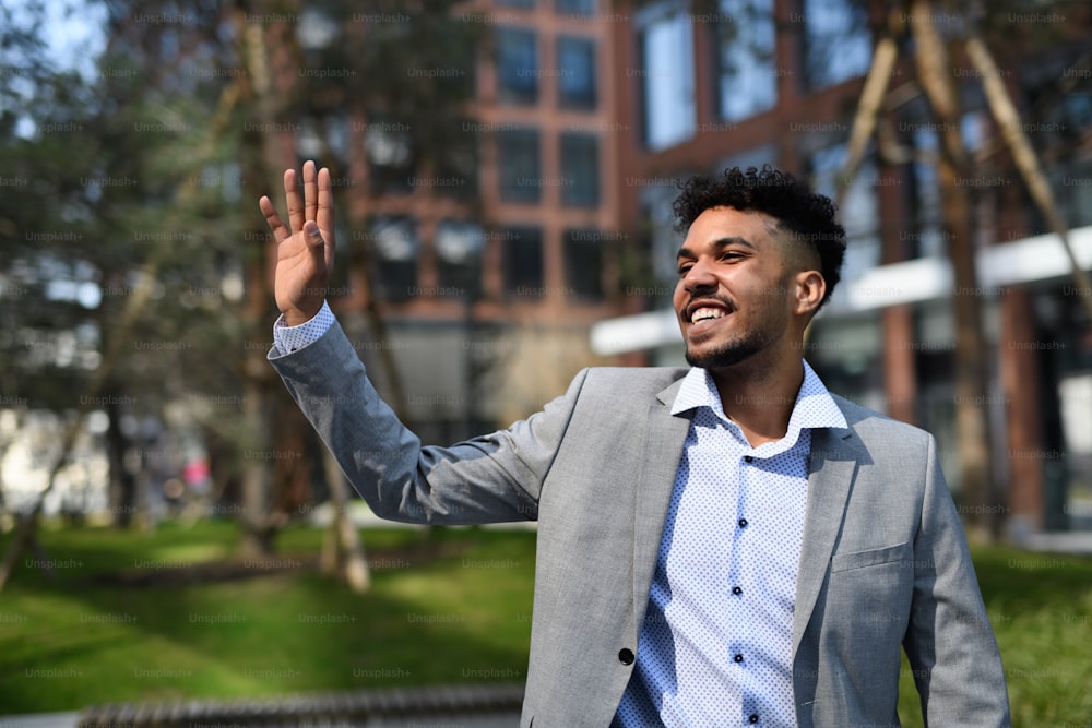 A portrait of young man student walking outdoors in city, greeting someone.
