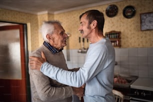 A portrait of man with elderly father indoors at home, shaking hands.