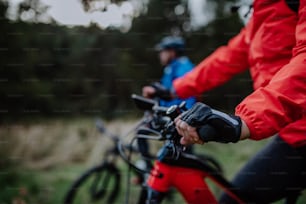 A detail of senior woman's hand riding bikes outdoors with her husband in forest in autumn day.