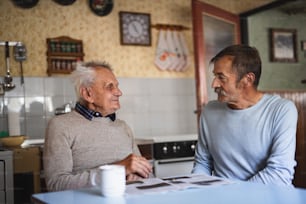 A portrait of man with elderly father sitting at the table indoors at home, talking.