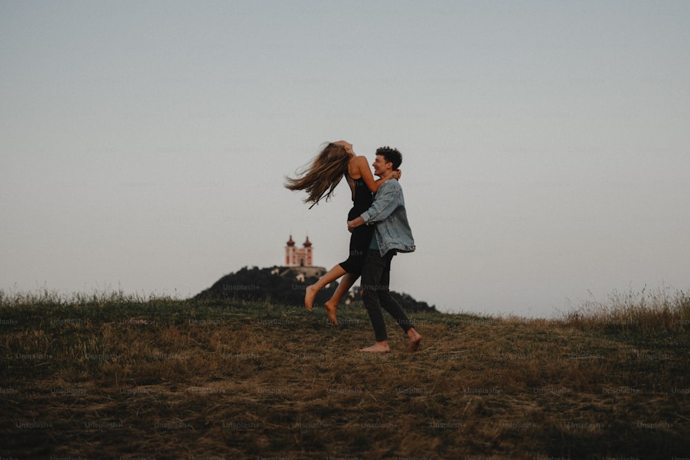 Side view of young couple on a walk in nature at dusk in countryside, having fun hugging.