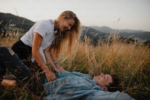 A young couple on a walk in nature in countryside, lying in grass laughing.