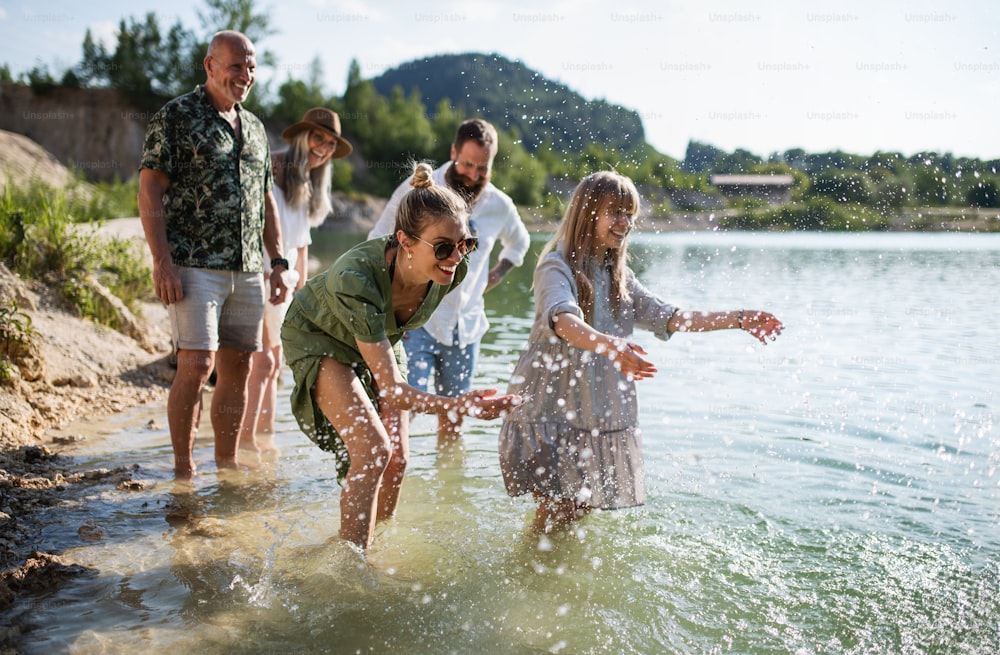 Une famille multigénérationnelle heureuse en promenade au bord du lac pendant les vacances d’été, s’amusant dans l’eau.