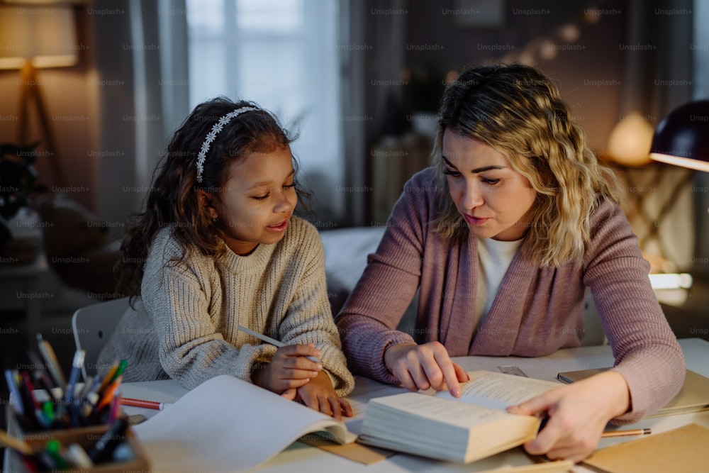 A little girl doing homework with her mother in evening at home.