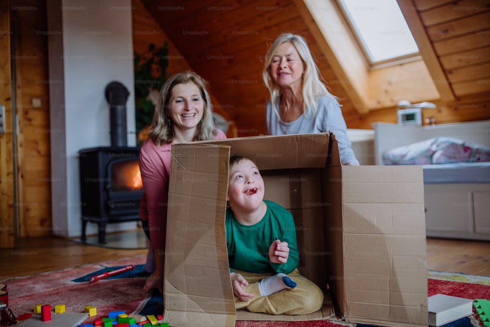 ダウン症の男の子と、母親と祖母が家で一緒に箱遊びをしている。