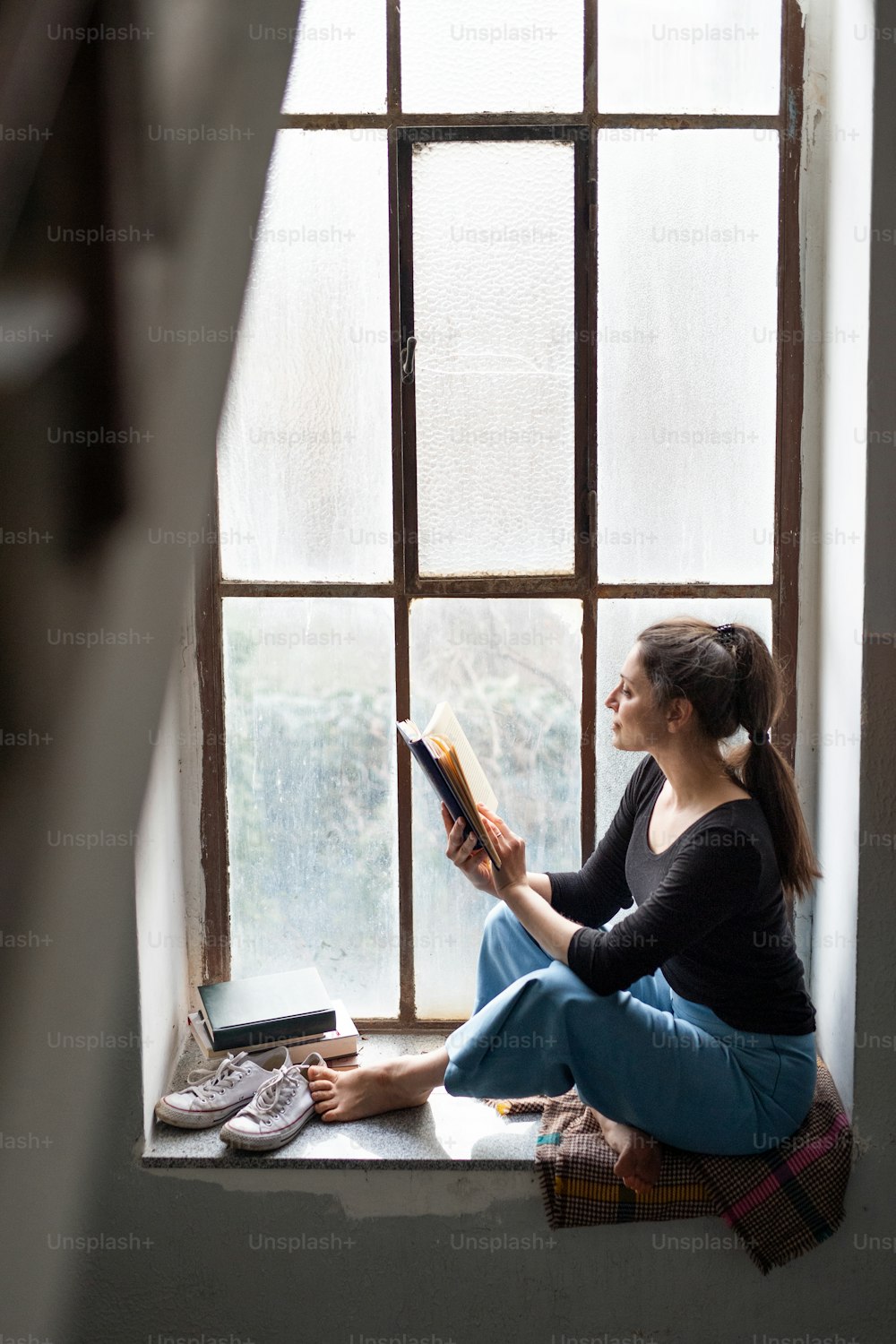 Portrait of happy woman sitting on old and dirty window sill, reading a book.