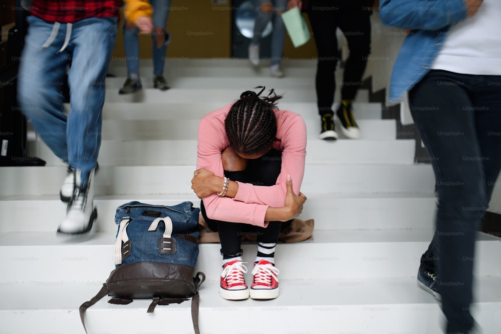 안면 마스크를 쓴 우울한 어린 학생이 대학이나 대학교에서 바닥에 앉아 공부하고 있습니다.