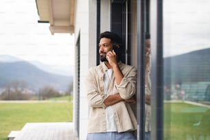 Portrait of young man student with smartphone outdoors on patio at home, making a phone call.