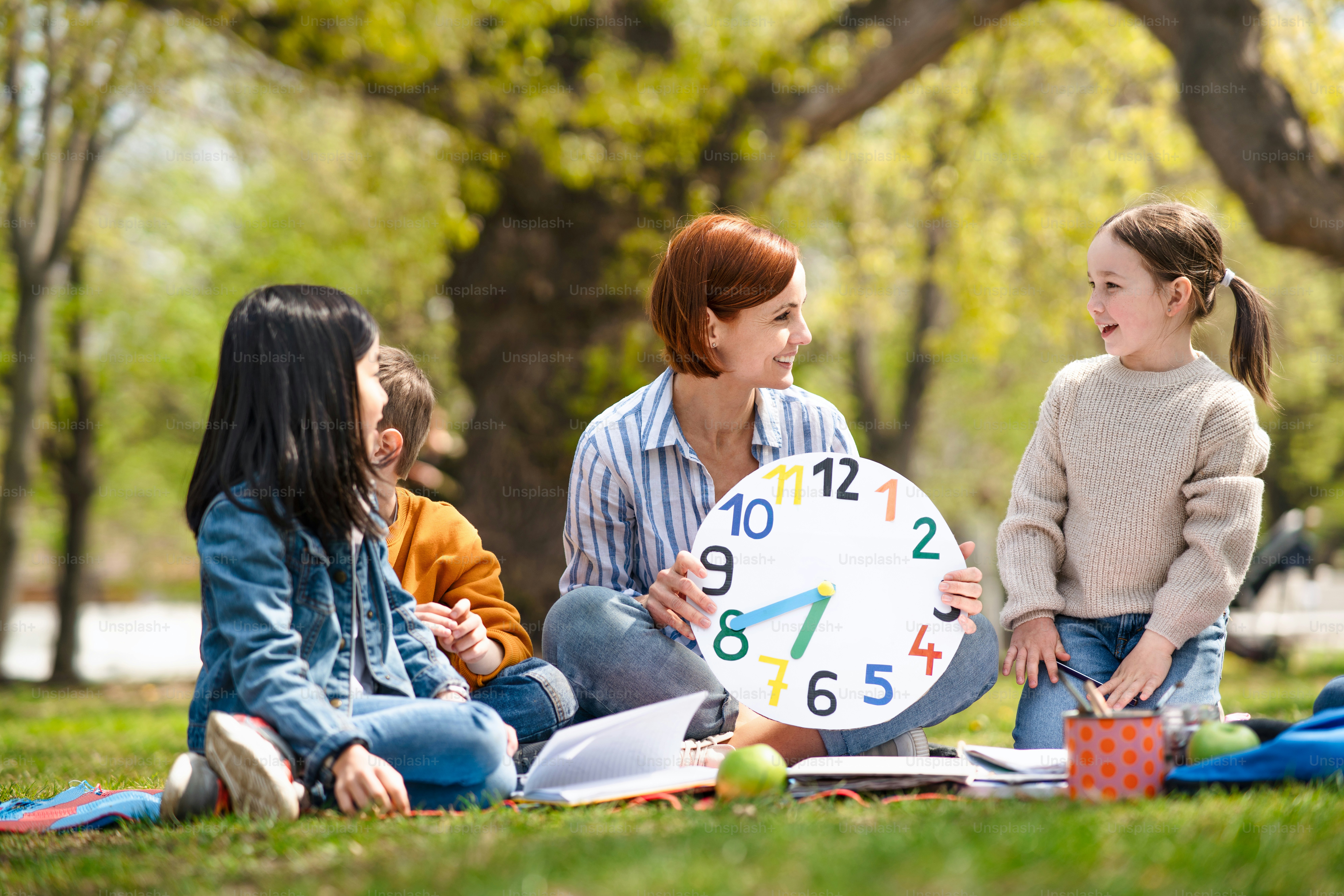 Um professor com crianças pequenas sentadas ao ar livre no parque da cidade, aprendendo conceito de educação em grupo