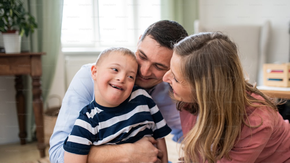 A cheerful down syndrome boy with parents indoors at home hugging.