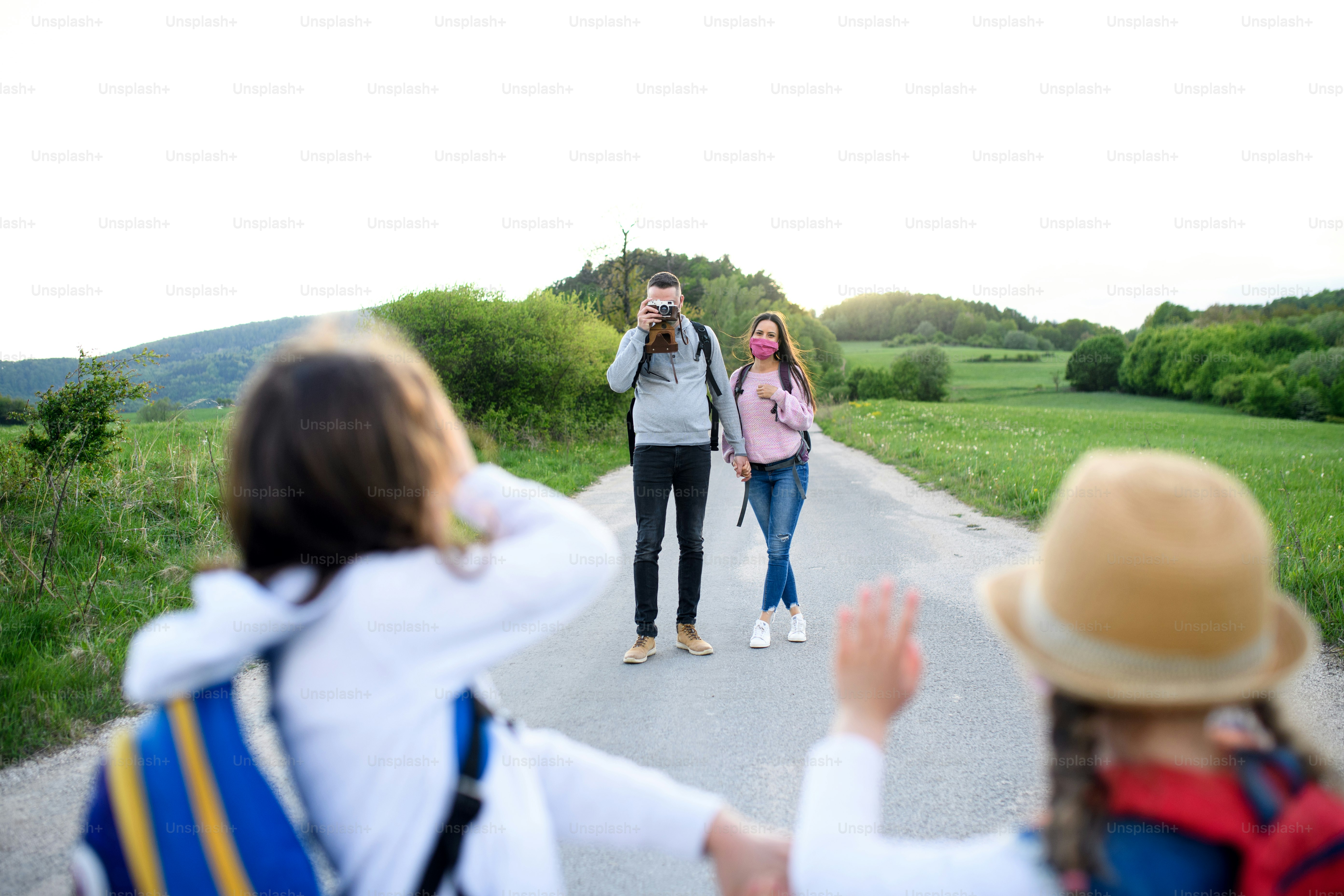 Front view of family with two small daughters on trip outdoors in nature, wearing face masks.