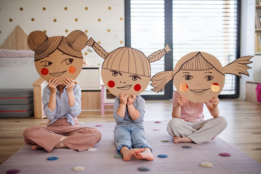 A portrait of three girls sisters indoors at home, playing.