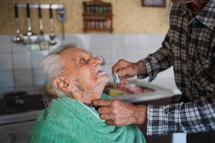 Retrato de hombre afeitando padre anciano feliz en el interior de la casa.
