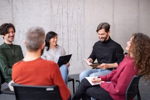 Happy men and women sitting in a circle during group therapy, reading and talking.