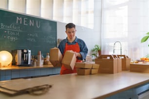 Un joven y alegre camarero con síndrome de Down que trabaja en un restaurante de comida para llevar, concepto de inclusión social.