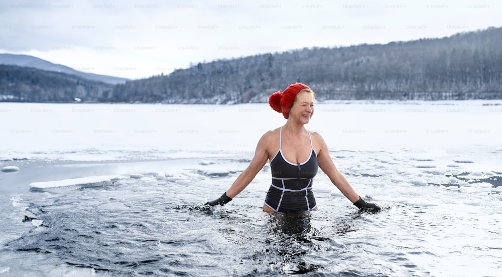 겨울에 물 속에서 야외에서 수영복을 입은 활동적인 노인 여성의 전면 모습, 감기 치료 개념.