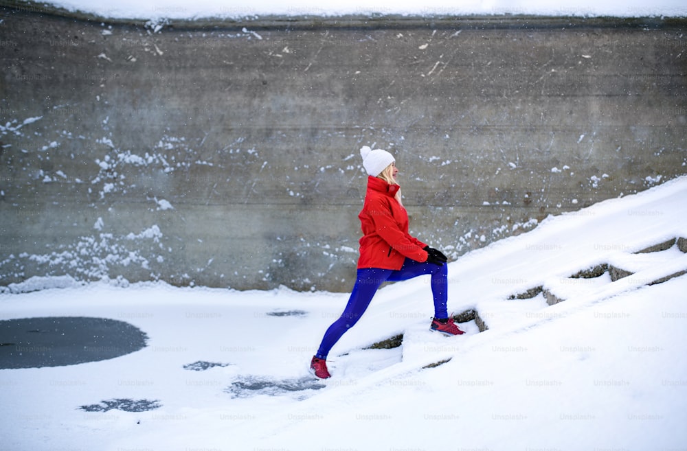 눈 덮인 겨울에 야외에서 운동을 하는 활동적인 노인 여성의 측면 모습.