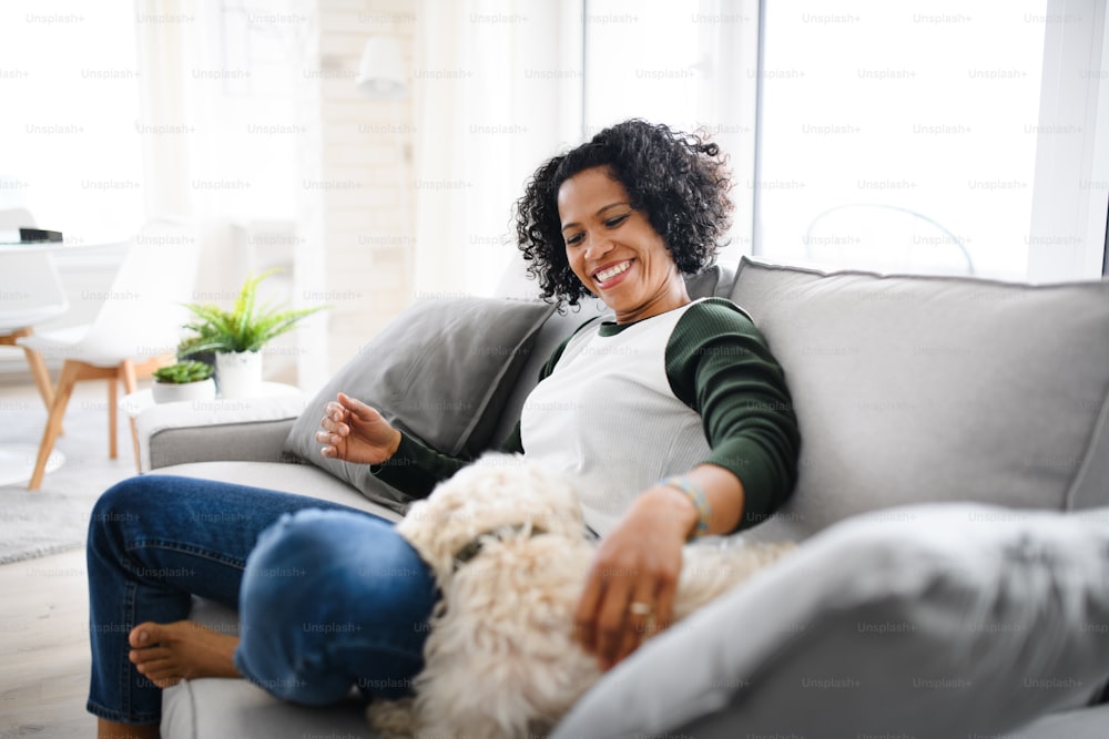 Um retrato de uma mulher madura feliz sentada dentro de casa, brincando com cachorro.