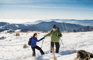 Senior couple with nordic walking poles hiking in snow-covered winter nature, healthy lifestyle concept.
