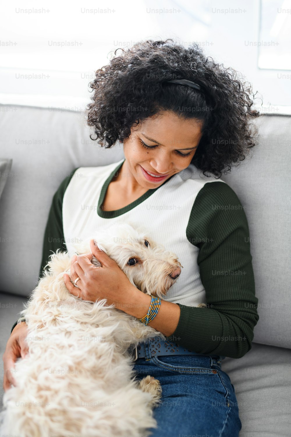 A portrait of happy mature woman sitting indoors at home, playing with dog.