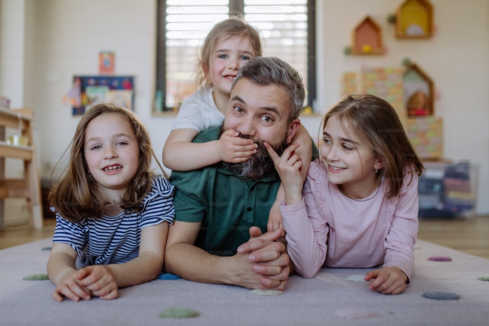 Un padre allegro con tre figlie piccole sdraiate insieme sul pavimento di casa.