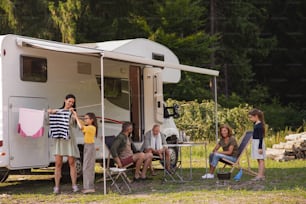 A mother with daughter hanging clothes by car outdoors in campsite, caravan family holiday trip.