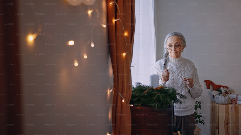 Uma mulher idosa acendendo vela na coroa de Natal dentro de casa em casa.