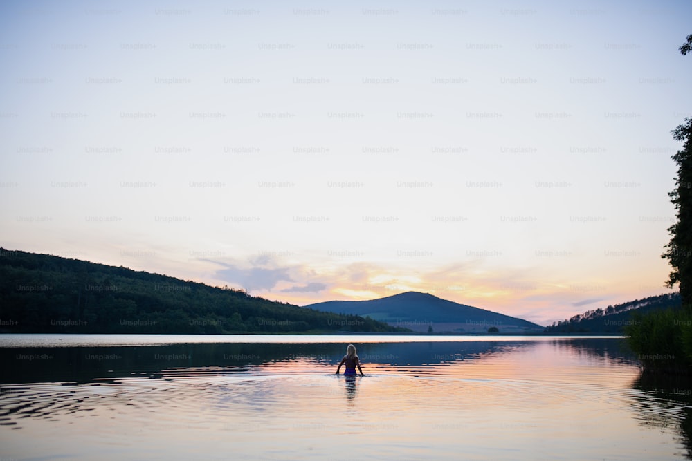 Une vue arrière d’une nageuse senior active plongeant à l’extérieur dans le lac, scène panoramique avec coucher de soleil