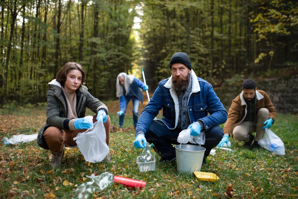 Un grupo de voluntarios mirando la cámara y limpiando el bosque de los desechos, concepto de servicio comunitario