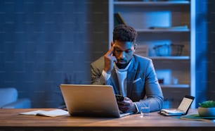 A young african american businessman working indoors in office at night.