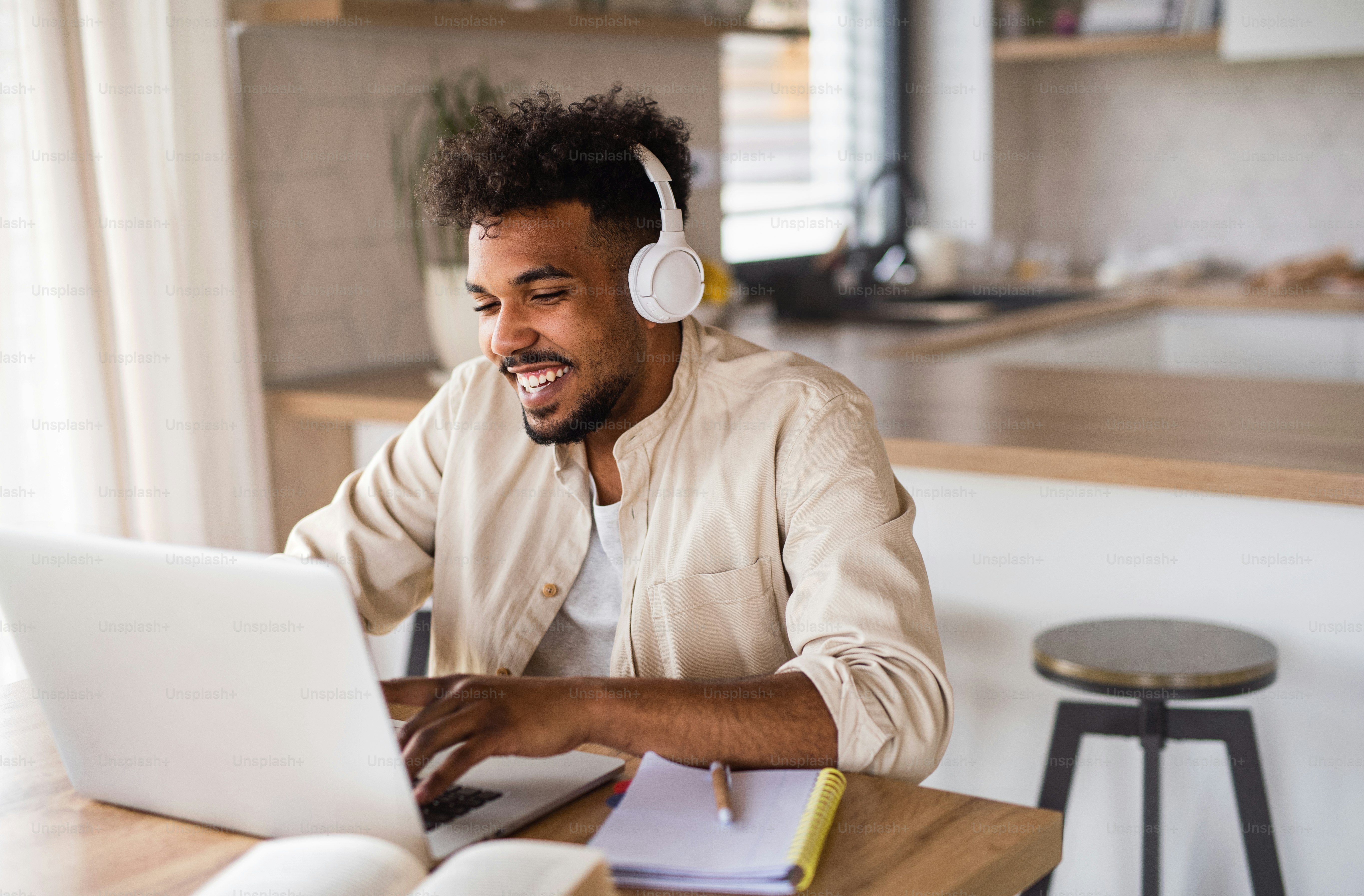 Potret siswa pemuda dengan laptop dan headphone di dalam ruangan di rumah, belajar.