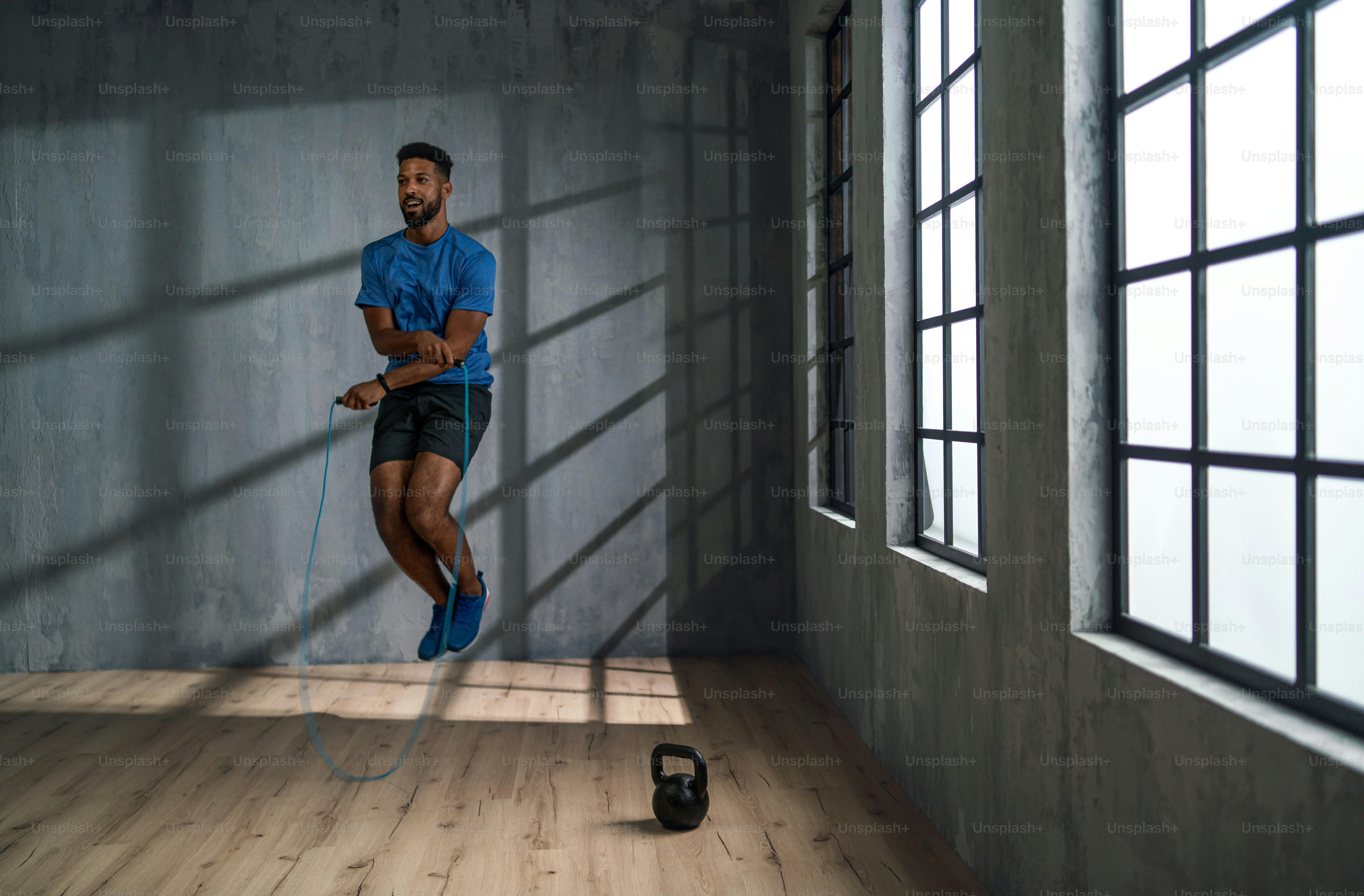 A young African American sportsman using jumping rope indoors, workout ...