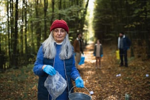 A senior woman volunteer looking at camera when cleaning up forest from waste, community service.