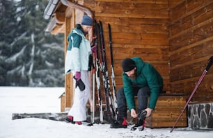 Couple d’âge mûr se reposant près d’une cabane en bois à l’extérieur dans la nature hivernale, ski de fond.