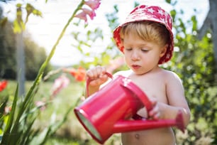 Unrecognizable small boy with can outdoors in garden in summer, watering flowers.