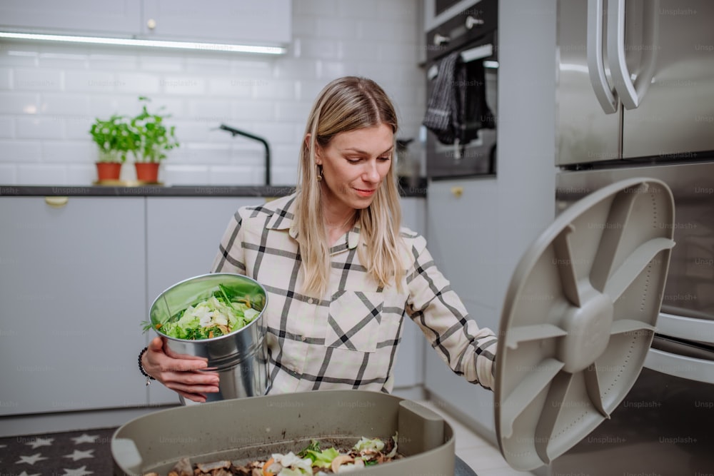 Une femme jetant des boutures de légumes dans un seau à compost dans la cuisine.