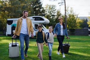 スーツケースを持って歩く幸せな若い家族、庭の屋外でのキャラバン旅行から帰宅