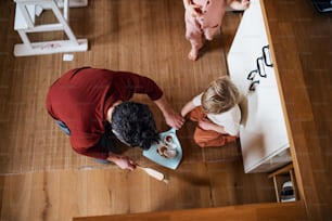 Eine Draufsicht von Vater mit kleinen Kindern, die zu Hause Scherben fegen, tägliches Aufgabenkonzept.