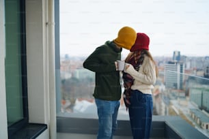 Feliz pareja joven propietaria con café en el balcón en un nuevo piso, mudanza, nuevo hogar y concepto de reubicación.