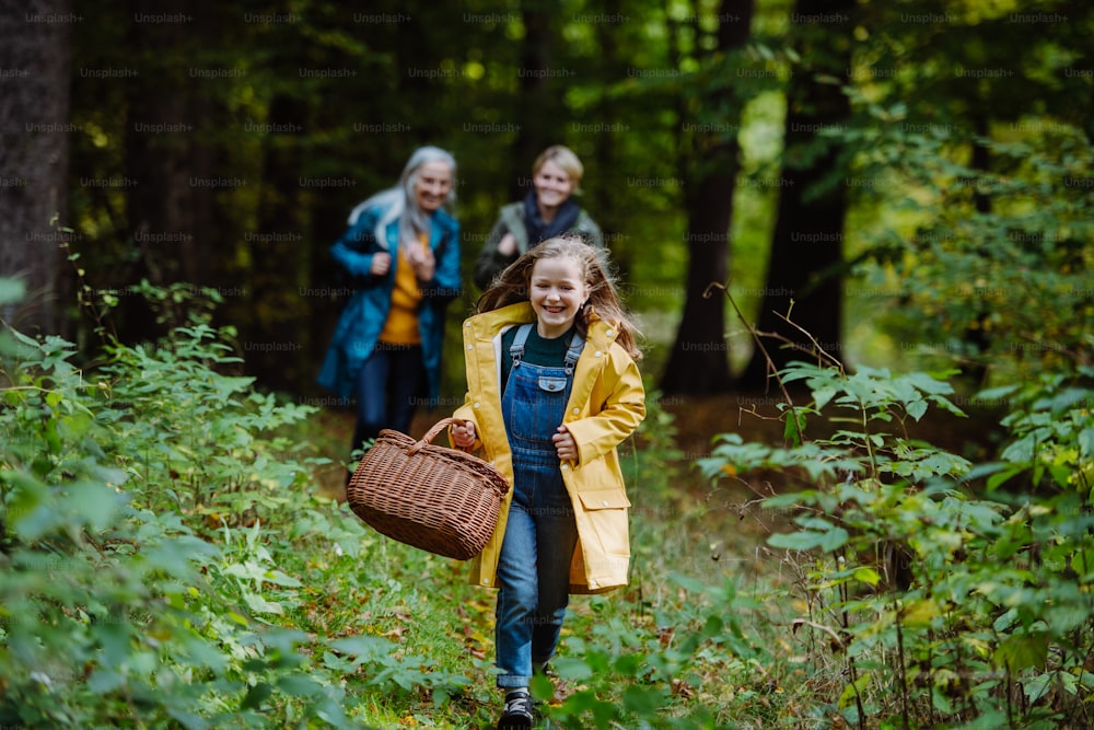 A happy little girl with basket running during walk with mother and grandmother outdoors in forest