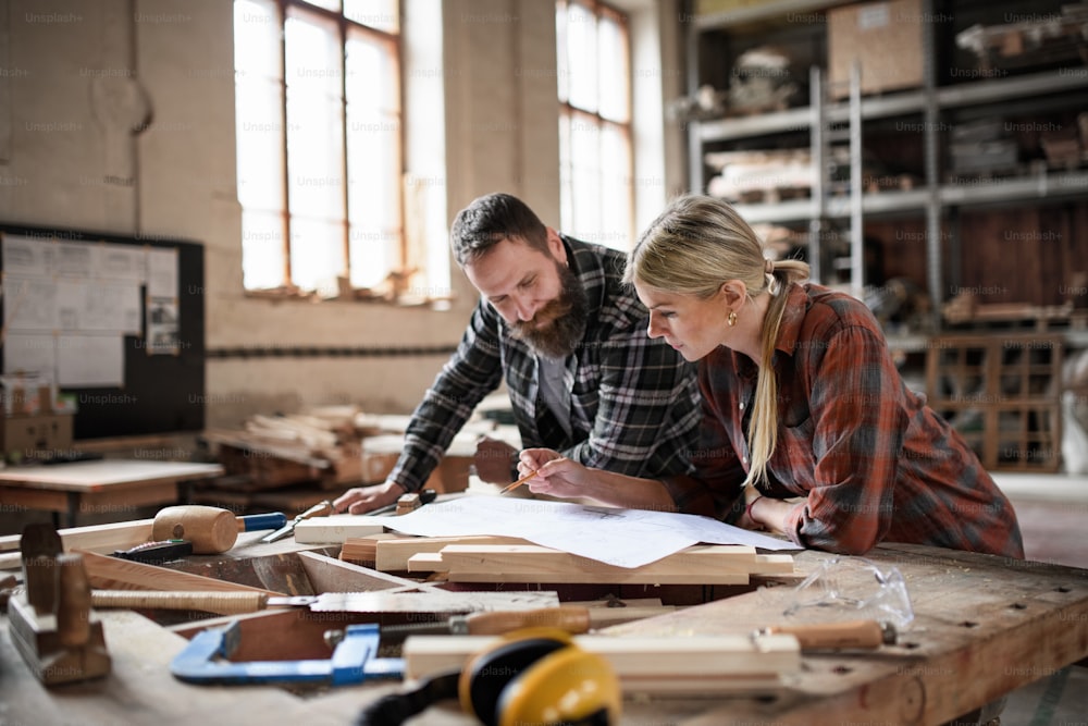Dos carpinteros, hombre y mujer, mirando planos en el interior de un taller de carpintería.