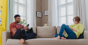 Joven pareja mixta adicta a los smartphones sentada en un sofá de su casa.